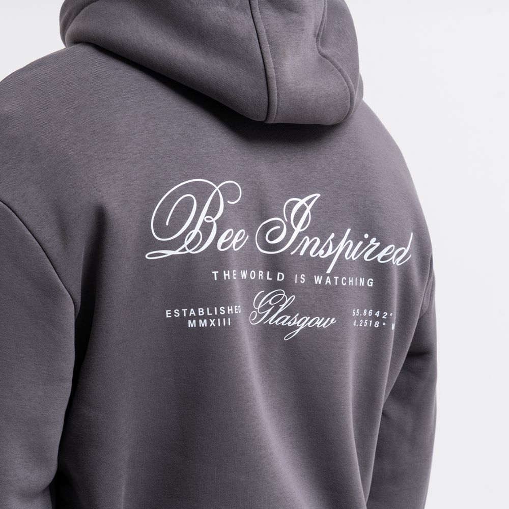 Grey hoodie with 'Bee Inspired' text on the back against a light gray background