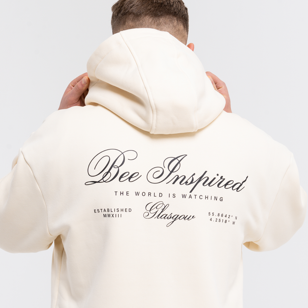 Person wearing a sand hoodie with 'Bee Inspired' text on the back against a white background