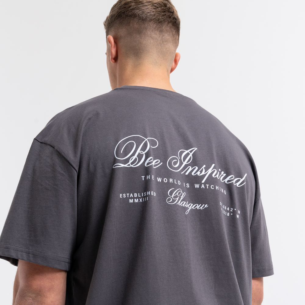 Person wearing a grey t-shirt with 'Bee Inspired' text on the back against a light grey background