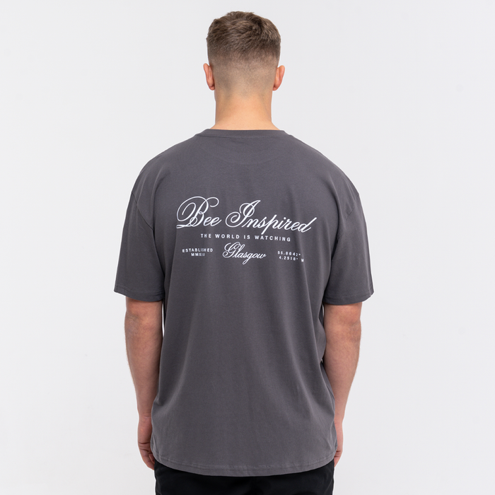 Person wearing a grey t-shirt with 'Bee Inspired' text on the back against a white background