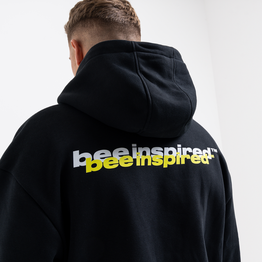 Person wearing a black hoodie with 'bee inspired' text on the back against a white background