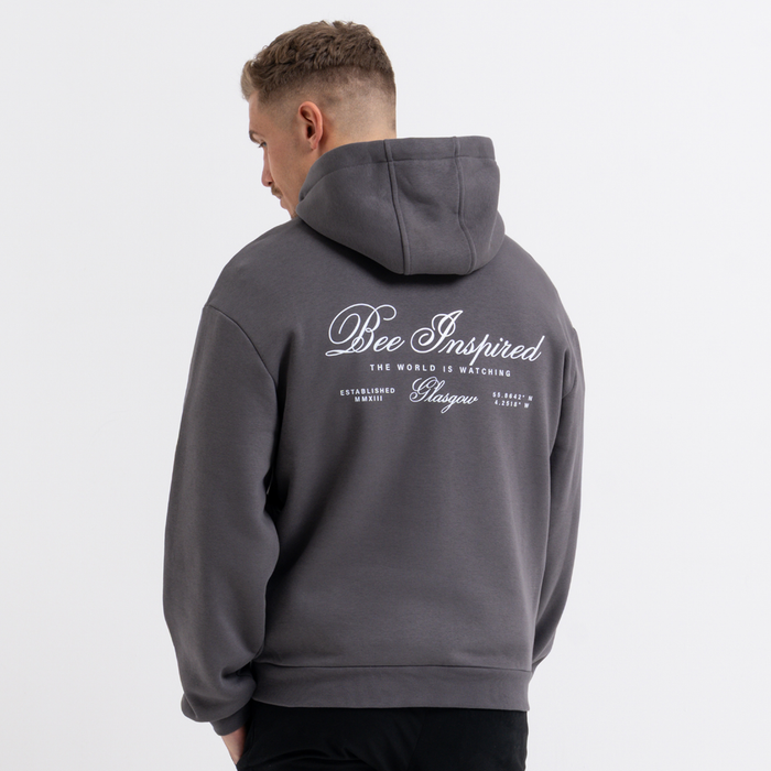 Person wearing a grey hoodie with 'Bee Inspired' text on the back against a white background