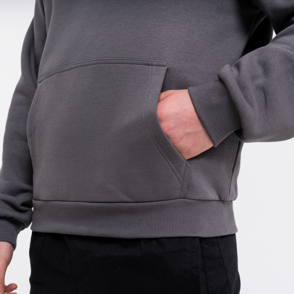 Person wearing a grey hoodie with a pocket, standing against a light grey background
