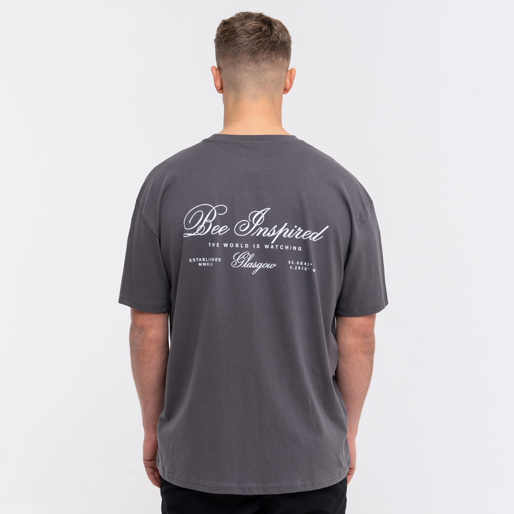 Person wearing a grey t-shirt with 'Bee Inspired' text on the back against a white background